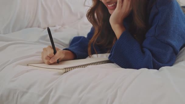 快乐的年轻女人躺在床上 在卧室写日记 — 图库视频影像