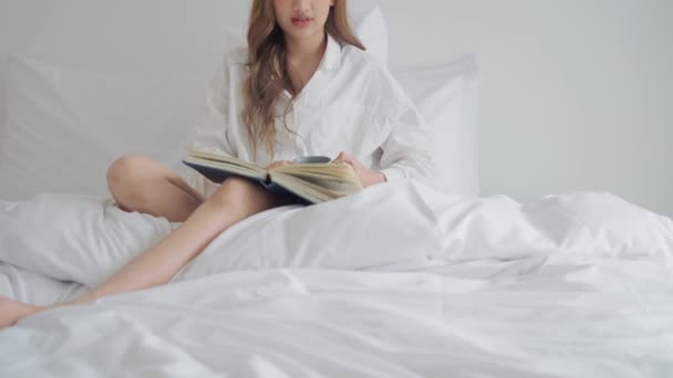 年轻的女人坐在床上看书 一边喝咖啡 — 图库视频影像
