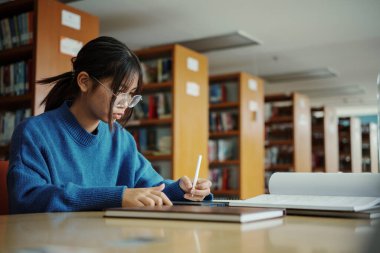 Stylus 'u olan kız öğrenci üniversite kütüphanesinde ödev yaparken tablet üzerinde veri tarıyor..