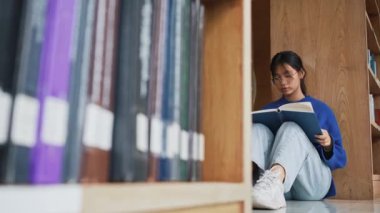Öğrenci kız kütüphanede yerde oturup kitap okuyor ve sınava hazırlanıyor. Eğitim ve öğrenme kavramı.
