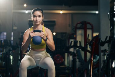 Genç kadın spor salonunda kettlebell ağırlık kaldırma sporuyla egzersiz yapıyor..