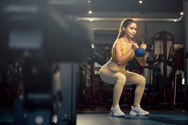 Genç kadın spor salonunda kettlebell ağırlık kaldırma sporuyla egzersiz yapıyor..