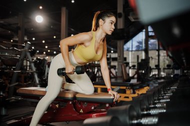 Fitness kızı spor salonunda dambılları kaldırır..