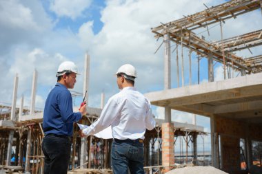 İnşaat alanında çalışan iki mühendis ve kontrol planı.