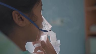 Hastanede oksijen maskesi takan ve nebulizatörle nefes alan Asyalı bir kız..