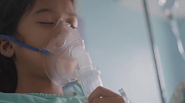 Hastanede oksijen maskesi takan ve nebulizatörle nefes alan Asyalı bir kız..