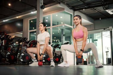 İki genç Asyalı kadın beden eğitimi antrenmanında kettlebell ağırlık kaldırıyor..