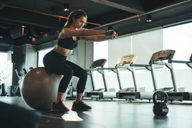 Sportif kadın spor yapıyor ve fitball 'u üzerinde oturarak ve dengede durarak kullanıyor..