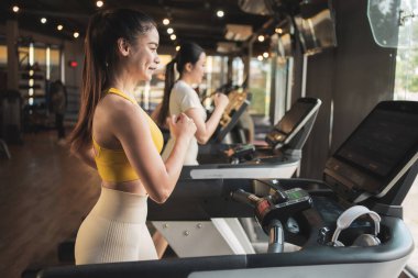 Spor salonunda spor yaparken iki genç kadın koşu bandında koşuyor..