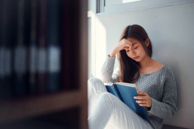 Genç Asyalı üniversite öğrencisi kütüphanede oturmuş kitap okuyor..