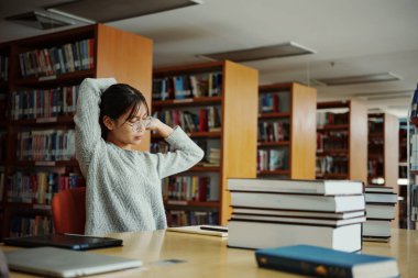 Genç Asyalı üniversite öğrencisi el ele tutuşup kütüphanedeki masasında dinleniyor..