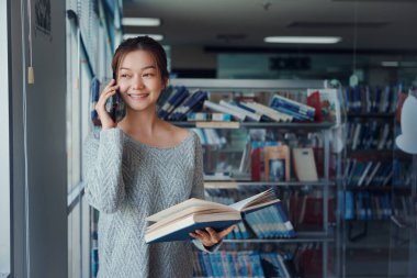 Kütüphanedeki genç Asyalı kadın kütüphanedeki arkadaşlarıyla konuşmak için telefonu kullanıyor..