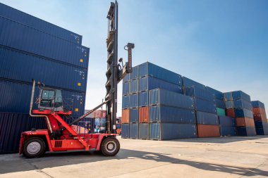 Lojistik nakliye sahasındaki yük konteynırlarını taşıyan forklift kamyonunun arka planında kargo konteynırları var..