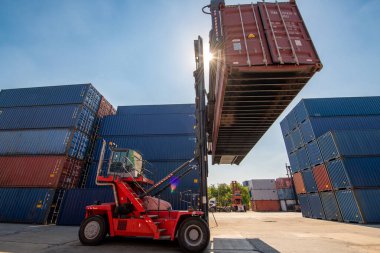 Lojistik nakliye sahasındaki yük konteynırlarını taşıyan forklift kamyonunun arka planında kargo konteynırları var..