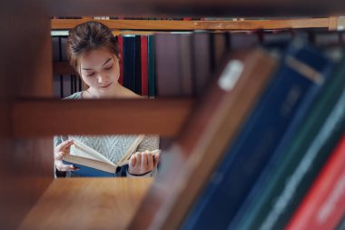 Eğitim, öğrenim ve araştırma için kütüphanede kitap okuyan Asyalı kadın okul, üniversite veya üniversite kampüsünde.