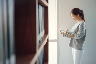 Eğitim, öğrenim ve araştırma için kütüphanede kitap okuyan Asyalı kadın okul, üniversite veya üniversite kampüsünde.