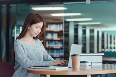Asyalı kadın öğrenci araştırma, öğrenim ve öğrenim için kütüphanede bilgi, bilgi ve edebiyat projeleri için ders kitapları ile notlar yazıyor..
