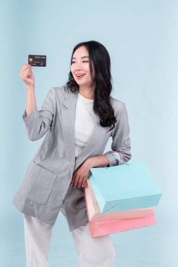 Genç Asyalı bir kadın alışveriş yaptıktan sonra paket çantalarını tutar ve açık mavi arka planda kredi kartını izole eder. Kara Cuma satış günü konsepti.