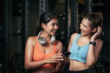 İki Asyalı kadın spor salonunda akıllı telefon kullanıyor..