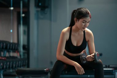 Spor salonunda spor yapan ve ağırlık kaldıran Asyalı genç bir kadın..