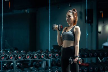 Spor salonunda spor yapan ve ağırlık kaldıran Asyalı genç bir kadın..