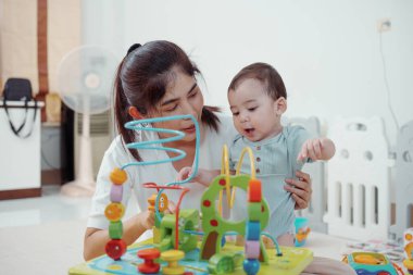 Tatlı Asyalı kadın ve küçük oğlu oturma odasında birlikte eğitici oyuncaklar oynuyorlar. Anne ve oğlu küp oynayıp gülüyorlar. Mutlu aile. Genç anne ve oğlu evde birlikte aktiviteler yapıyorlar..