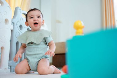 Evde çocuklarla oynayan sevimli, mutlu bir bebek. Oturma odasında yerde oturuyor..