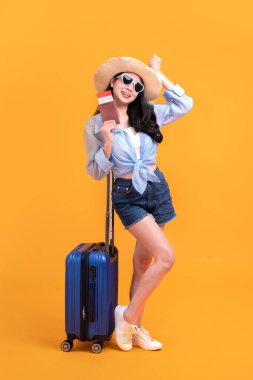 Pasaportu ve bavulu olan mutlu Asyalı genç turist kadın turuncu arka planda izole bir şekilde tatile çıkıyor..