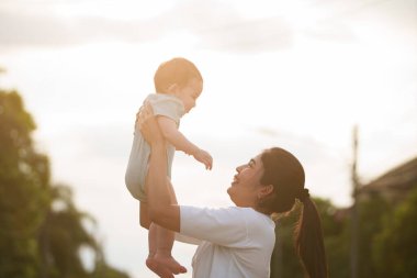 Dışarıda mutlu bir aile. Anne dışarıda çocuğunu kucaklıyor. Anne bebeğini kucağında tutuyor. Anne bebeğine sevgi ve özenle sarılıyor..