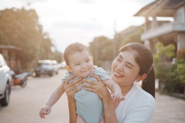 Dışarıda mutlu bir aile. Anne dışarıda çocuğunu kucaklıyor. Anne bebeğini kucağında tutuyor. Anne bebeğine sevgi ve özenle sarılıyor..