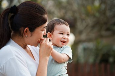 Dışarıda mutlu bir aile. Anne dışarıda çocuğunu kucaklıyor. Anne bebeğini kucağında tutuyor. Anne bebeğine sevgi ve özenle sarılıyor..