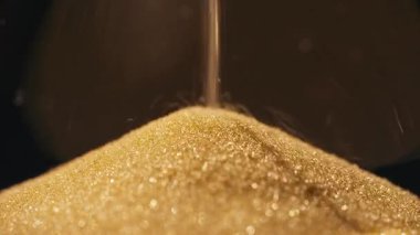 Kum saatinden sızan altın parıltılı kumun yakın plan fotoğrafı..