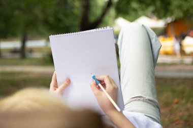 Anonymous girl making notes or drawing in the blank paper book.