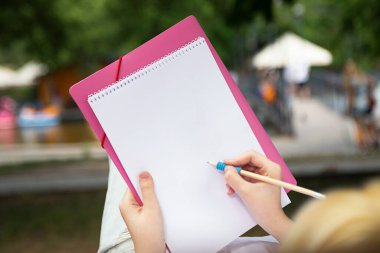 Anonymous girl making notes or drawing in the blank paper book.