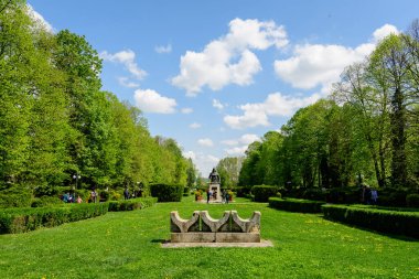 Targoviste, Romanya, 1 Mayıs 2022: Beyaz bulutlar ve mavi gökyüzü ile güneşli bir bahar gününde Chindia Park 'ta (Parcul Chindia) canlı yeşil ağaçlar ve çimlerle kaplı manzara