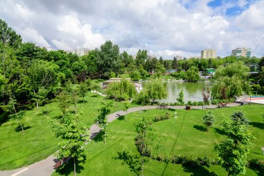 Romanya 'nın Bükreş kentindeki Moghioros Parkı olarak da bilinen Drumul Taberei Parkı' nda (Parcul Drumul Taberei), bulutlu bir yaz gününde göl ve canlı yeşil ağaçlarla çevrili manzara