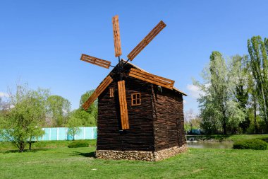 Romanya 'nın Targoviste kentindeki Chindiei Parkı (Parcul Chindiei) gölündeki küçük bir adada güneşli bir bahar gününde dekoratif eski ahşap değirmeni ve yeşil çimen