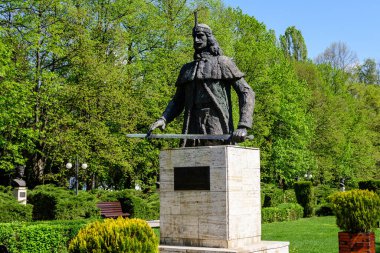 Romanya 'nın Targoviste şehrinden, beyaz bulutlar ve mavi gökyüzü ile güneşli bir bahar gününde, Chindia Park' taki (Parcul Chindia) canlı yeşil ağaçlar ve çimlerle kaplı manzara