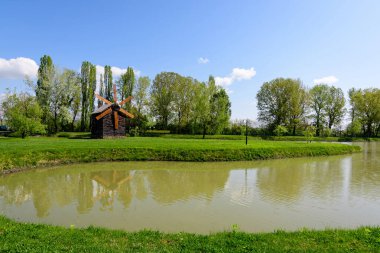 Small lake with a woodmill and an island from Chindiei Park (Parcul Chindiei) in Targoviste, Romania, in a sunny spring day with white clouds and blue sky clipart