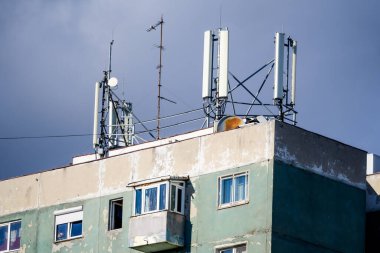 Telekomünikasyon antenleri arka planda bulutlu mavi gökyüzü olan eski bir binanın çatısında
