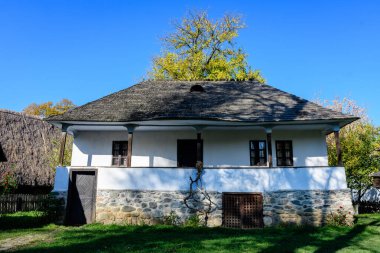 Romanya 'nın geleneksel evi, güneşli bir sonbahar gününde Romanya' nın Herastrau Park kentindeki Köy Müzesi 'nde yeşil, sarı, turuncu ve kahverengi yapraklı çok sayıda eski ağaçla çevrili.
