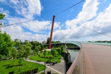 Romanya 'nın Bükreş kentinde, bulutlu bir yaz gününde Drumul Taberei Parkı' ndaki (Parcul Drumul Taberei) modern metalik, ahşap ve cam köprüye (Parcul Drumul Taberei) sahip manzara