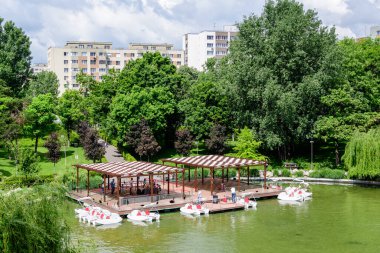 Bükreş, Romanya - 29 Mayıs 2021: Romanya 'nın Bükreş kentindeki Moghioros Parkı olarak da bilinen Drumul Taberei Parkı' ndaki göl ve canlı yeşil ağaçlarla manzara bulutlu bir yaz gününde