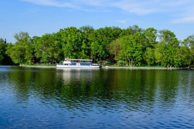Romanya 'nın Bükreş kentindeki Kral I. Michael Parkı' nda (eski Herastrau) güneşli bir sonbahar gününde, Herastrau Gölü 'ndeki beyaz tekneler ve büyük yeşil ağaçlarla manzara