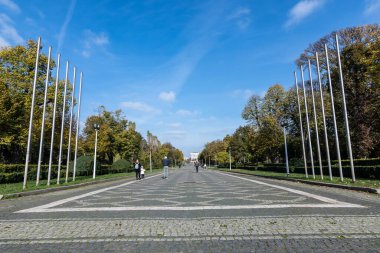 Romanya 'nın Bükreş kenti Parcul Carol' da (Carol Park) güneşli bir sonbahar gününde, büyük yaşlı ağaç dalları üzerinde yeşil, sarı, turuncu ve kahverengi yapraklarla çevrili ana caddenin manzarası