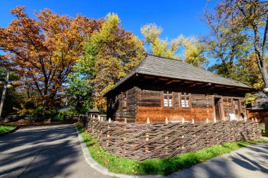 Romanya 'nın geleneksel evi, güneşli bir sonbahar gününde Romanya' nın Herastrau Park kentindeki Köy Müzesi 'nde yeşil, sarı, turuncu ve kahverengi yapraklı çok sayıda eski ağaçla çevrili.