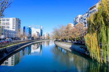 Bucharest, Romania, 20 November 2021: Modern buildings and offices near Dambovita river and cloudy blue sky in the center of the city, in a sunny autumn day