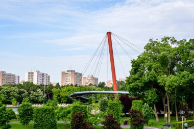 Romanya 'nın Bükreş kentindeki Moghioros Park olarak da bilinen Drumul Taberei Parkı' ndaki çağdaş kırmızı metalik köprü ve canlı yeşil çimen ve ağaçlarla (Parcul Drumul Taberei) manzara