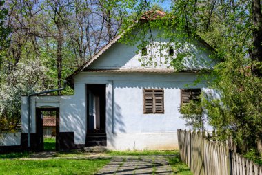 Bükreş, Romanya - 25 Nisan 2021: Eski geleneksel Romen evi güneşli bir bahar gününde Herastrau Park 'taki Dimitrie Gusti Ulusal Köy Müzesi' nde çok sayıda eski ağaç ve yeşil çimlerle çevrili