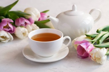 Beyaz bardakta güzel kokulu çay, çaydanlık ve parlak bir masada bir buket taze lale. Çay konsepti. Yakın plan. Seçici odak.